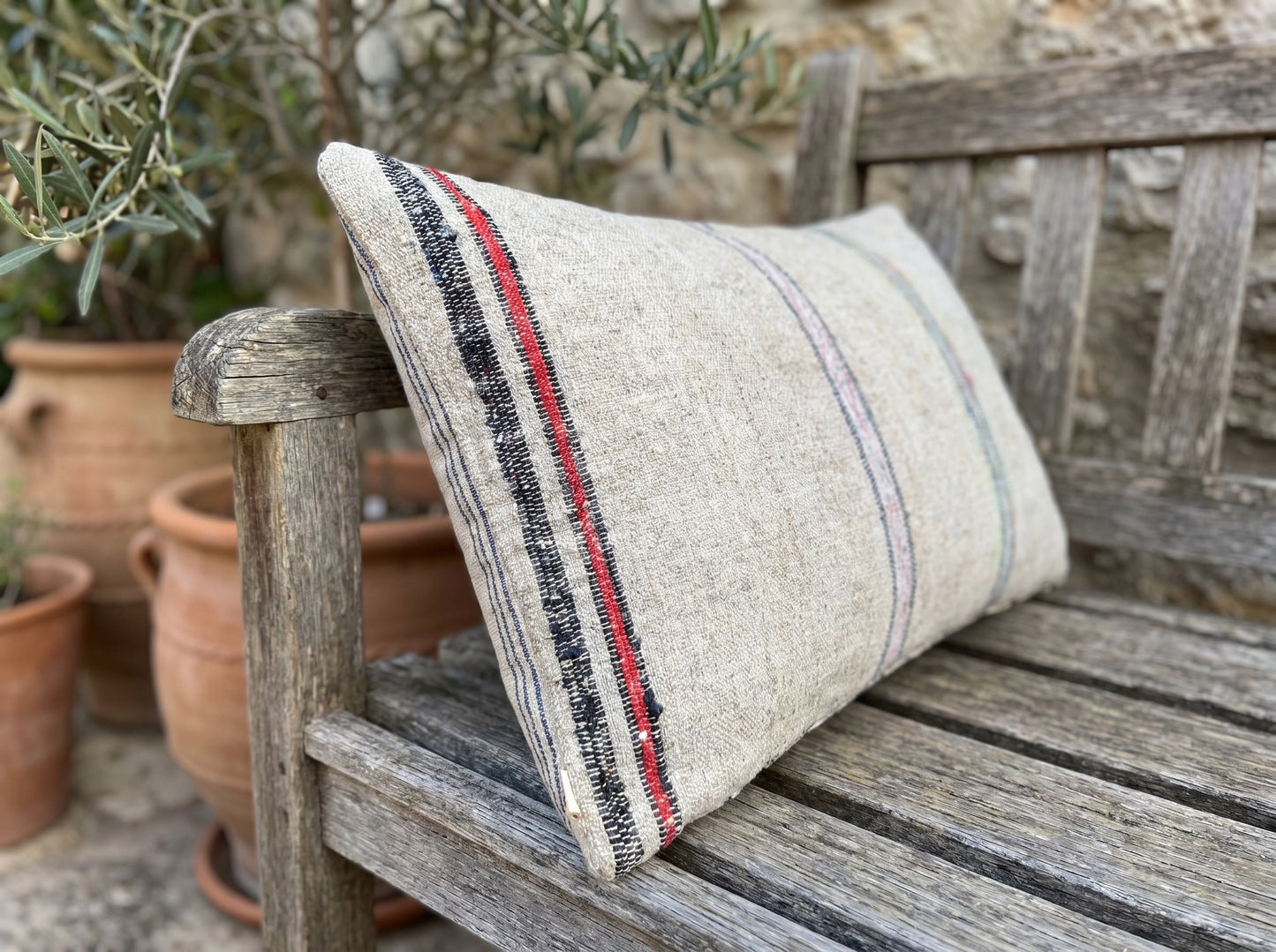A one-of-a-kind lumbar pillow crafted from authentic antique Anatolian grain sack textile with handwoven linen texture and faded multi-stripe detailing