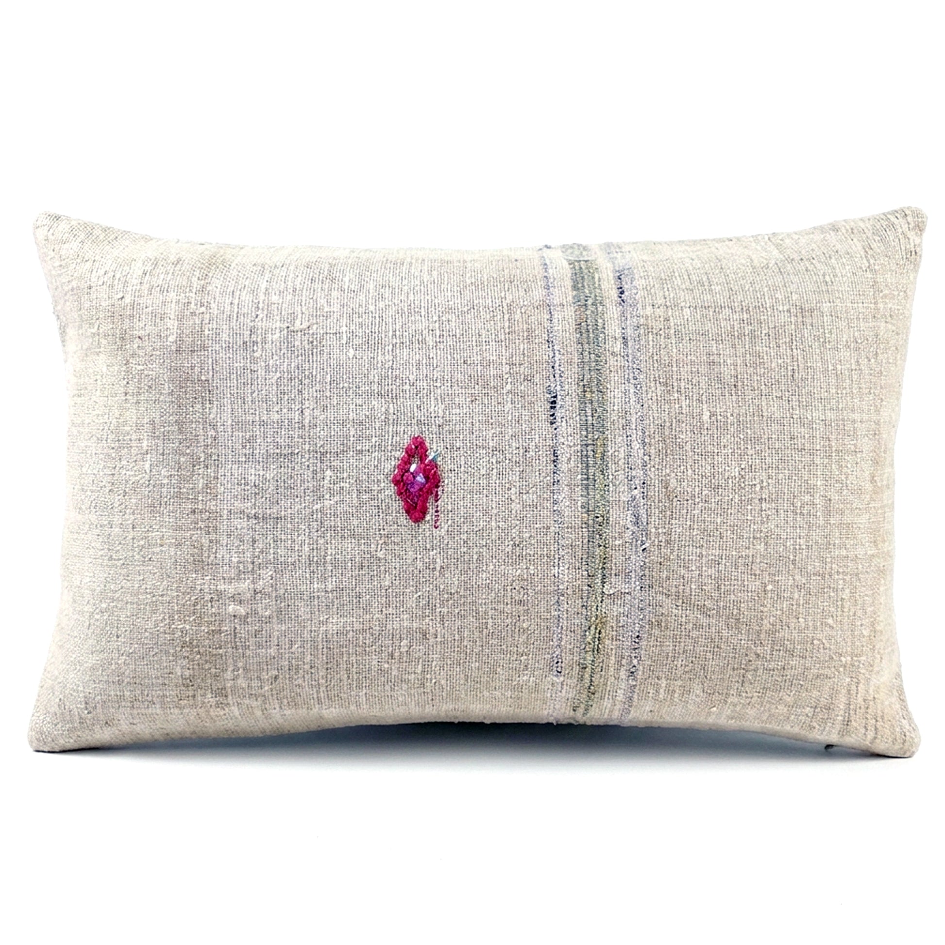 A rectangular lumbar throw pillow made of textured beige linen fabric, featuring a vertical stripe pattern in muted blue and green tones and a small magenta embroidered diamond on the front, set against a plain white background.