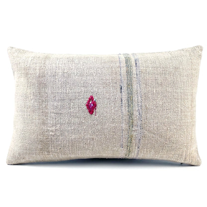 A rectangular lumbar throw pillow made of textured beige linen fabric, featuring a vertical stripe pattern in muted blue and green tones and a small magenta embroidered diamond on the front, set against a plain white background.