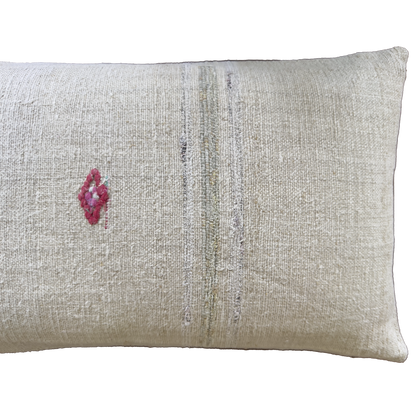 A rectangular beige linen throw pillow with a small pink embroidered diamond on the left and vertical distressed stripes in muted gray and olive tones.