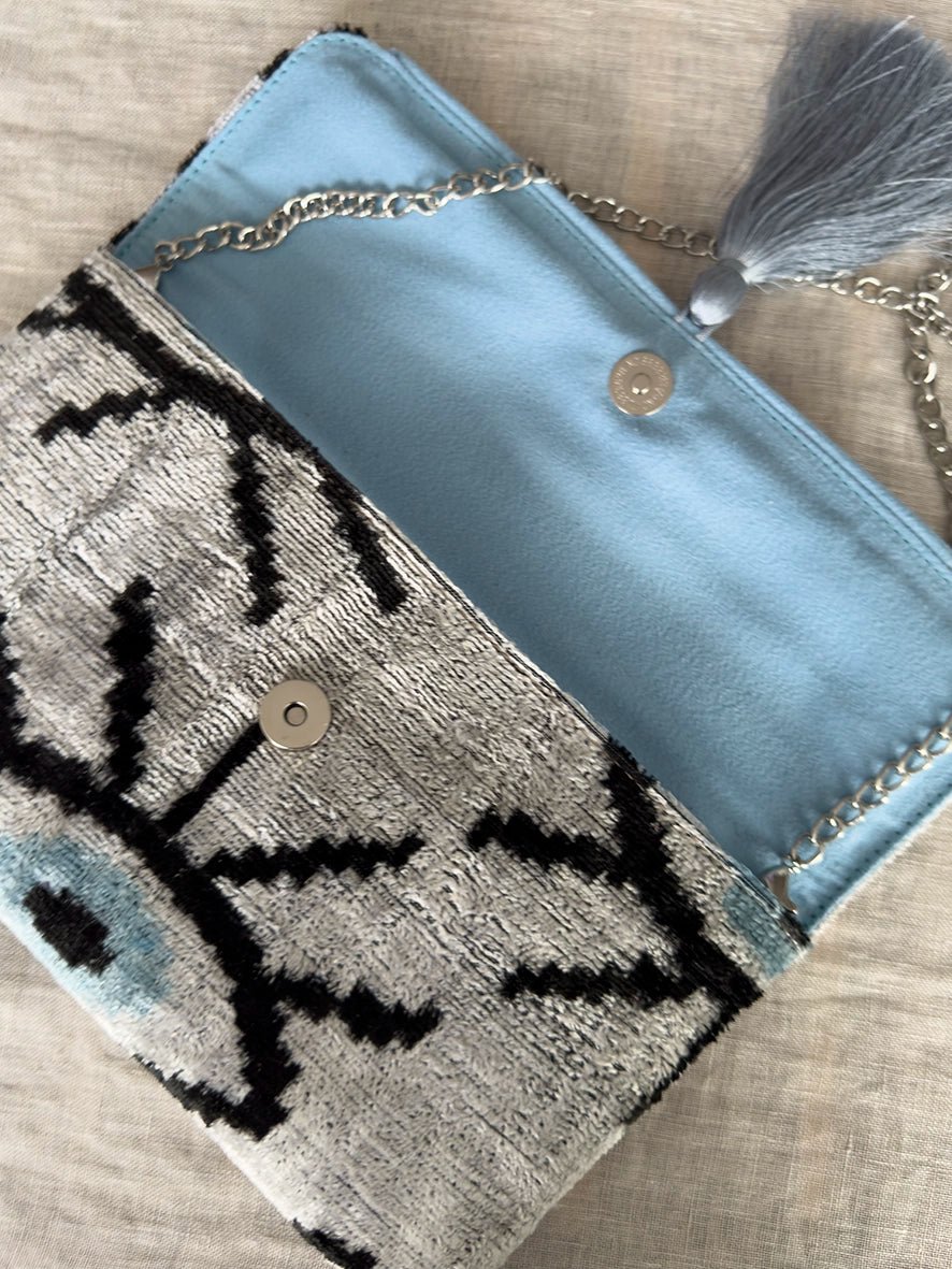 Blue and gray blue evil eye patterned clutch bag with chain strap on a wooden surface