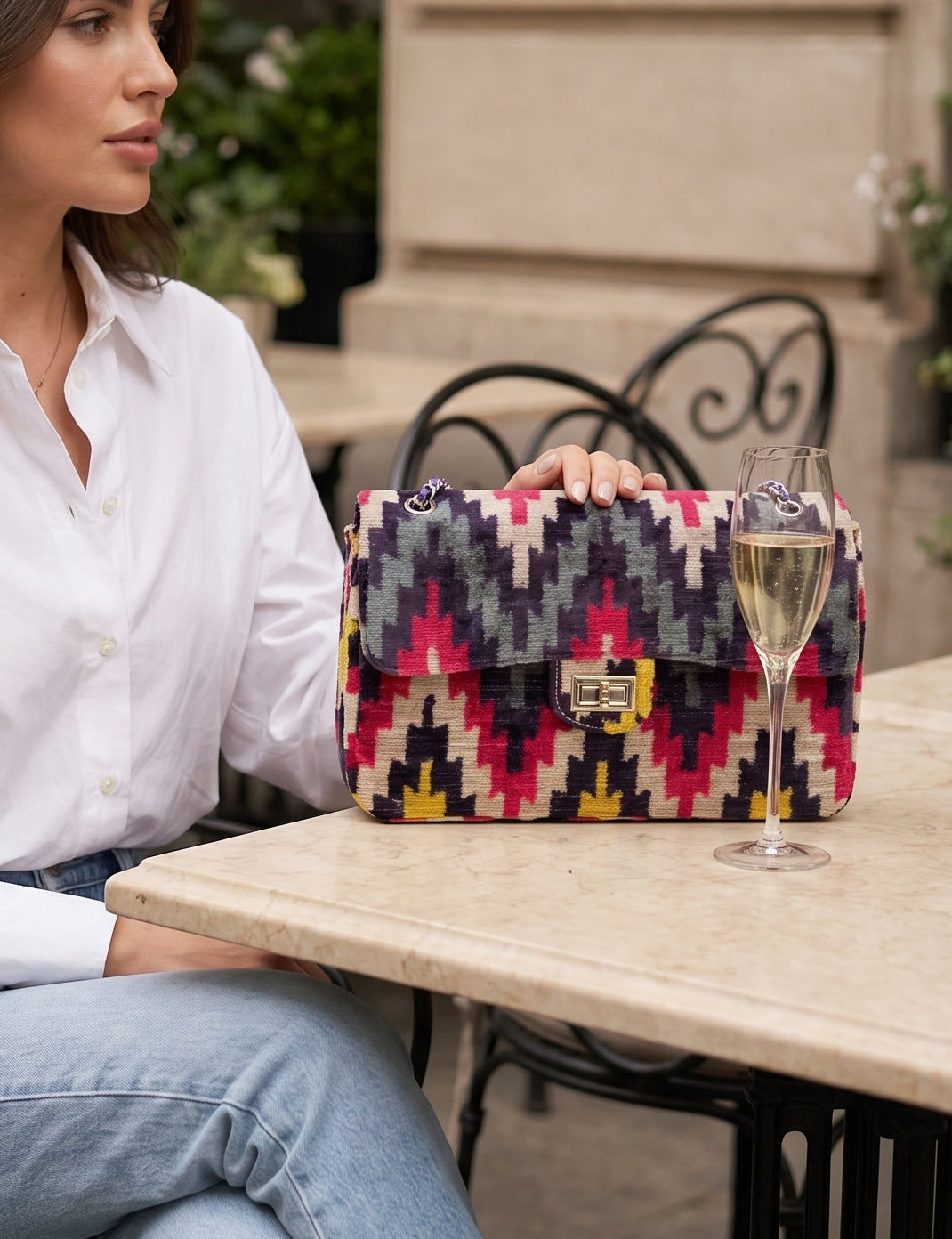 Woman sitting at an outdoor table with a colorful patterned handbag and a glass of champagne.