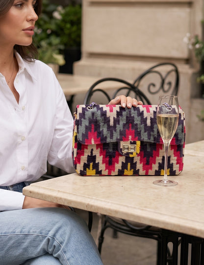 Woman sitting at an outdoor table with a colorful patterned handbag and a glass of champagne.