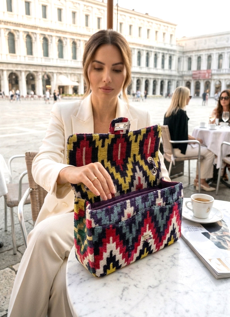 Woman sitting at an outdoor cafe table with a colorful patterned handbag.