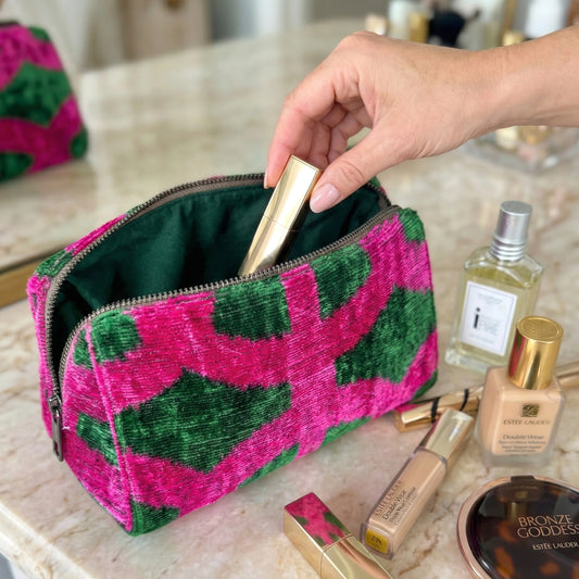 Person reaching into a pink and green patterned makeup bag on a marble surface with beauty products.