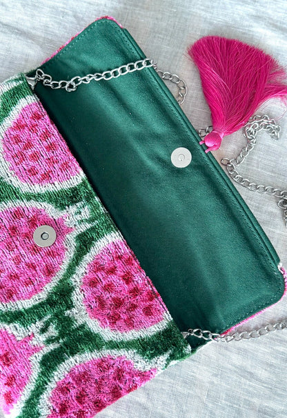Green and pink clutch bag with pink tassel and chain on a textured surface