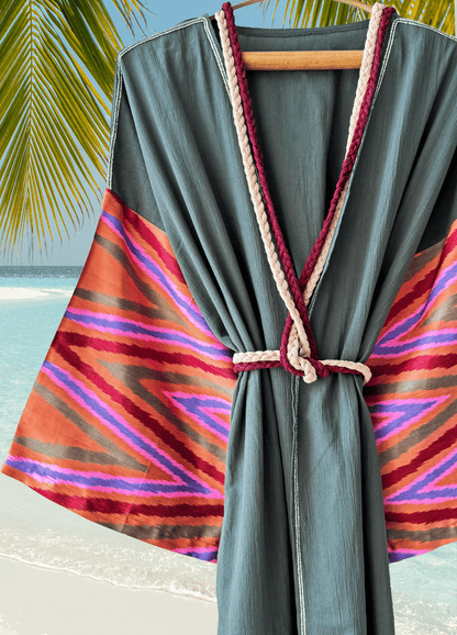 Green muslin robe with colorful striped silk ikat sleeves on a hanger against a beach background