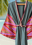 Green muslin robe with colorful striped silk ikat sleeves on a hanger against a beach background