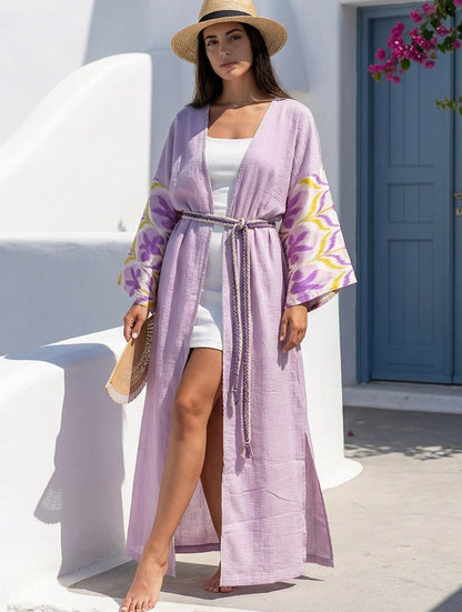 Woman in a lavender silk ikat sleeves dress with a straw hat standing in front of a white building with a blue door.