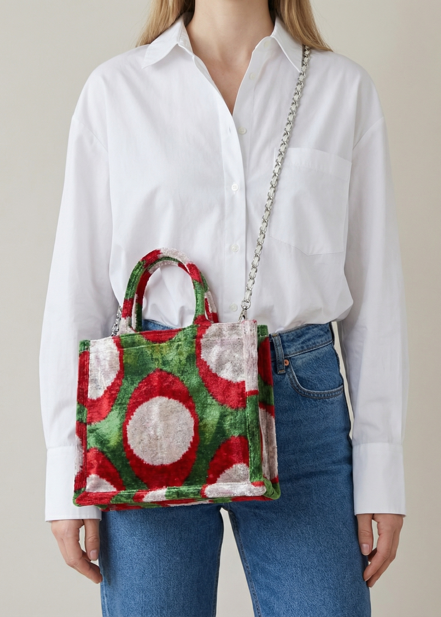 Person wearing a white shirt and blue jeans holding a colorful handbag with a pattern of red and green shapes.